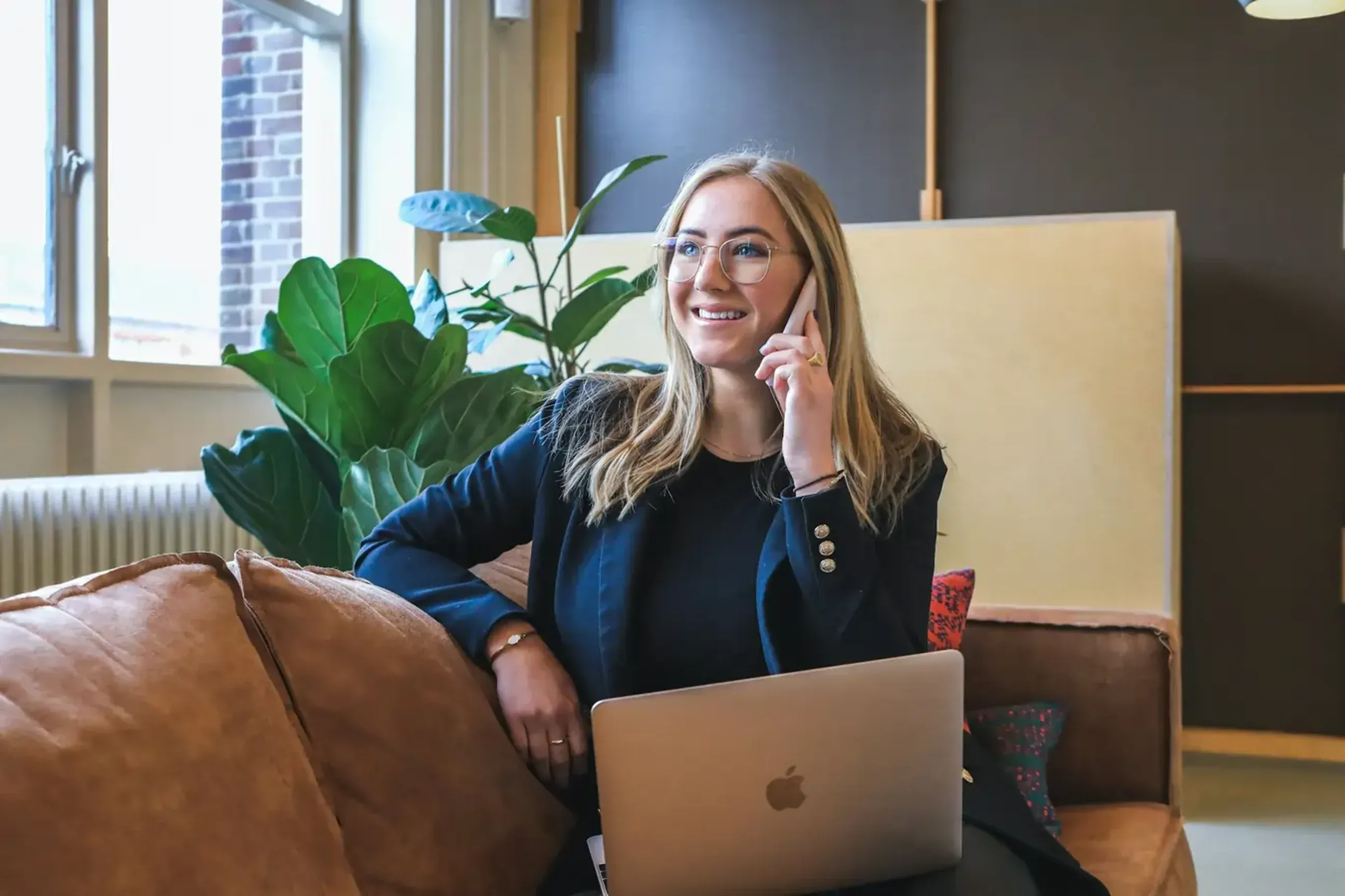 Woman sitting on couch with laptop making a phone call.