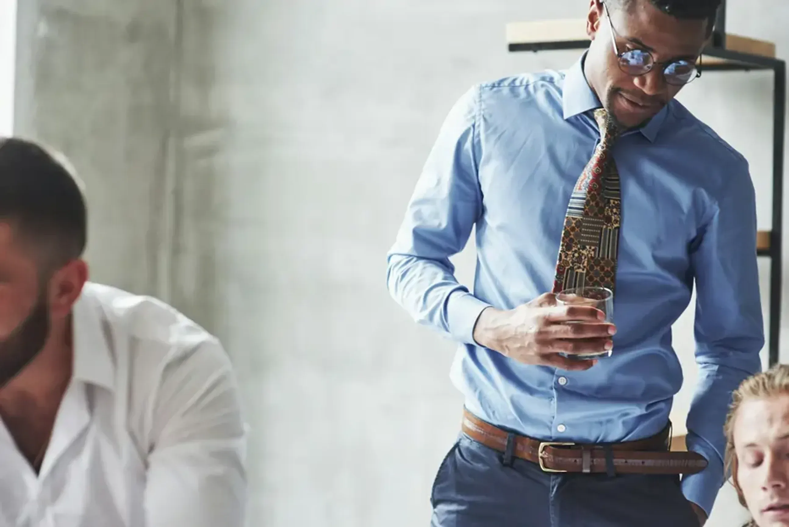 Man in an office holding a glass while talking to coworkers.