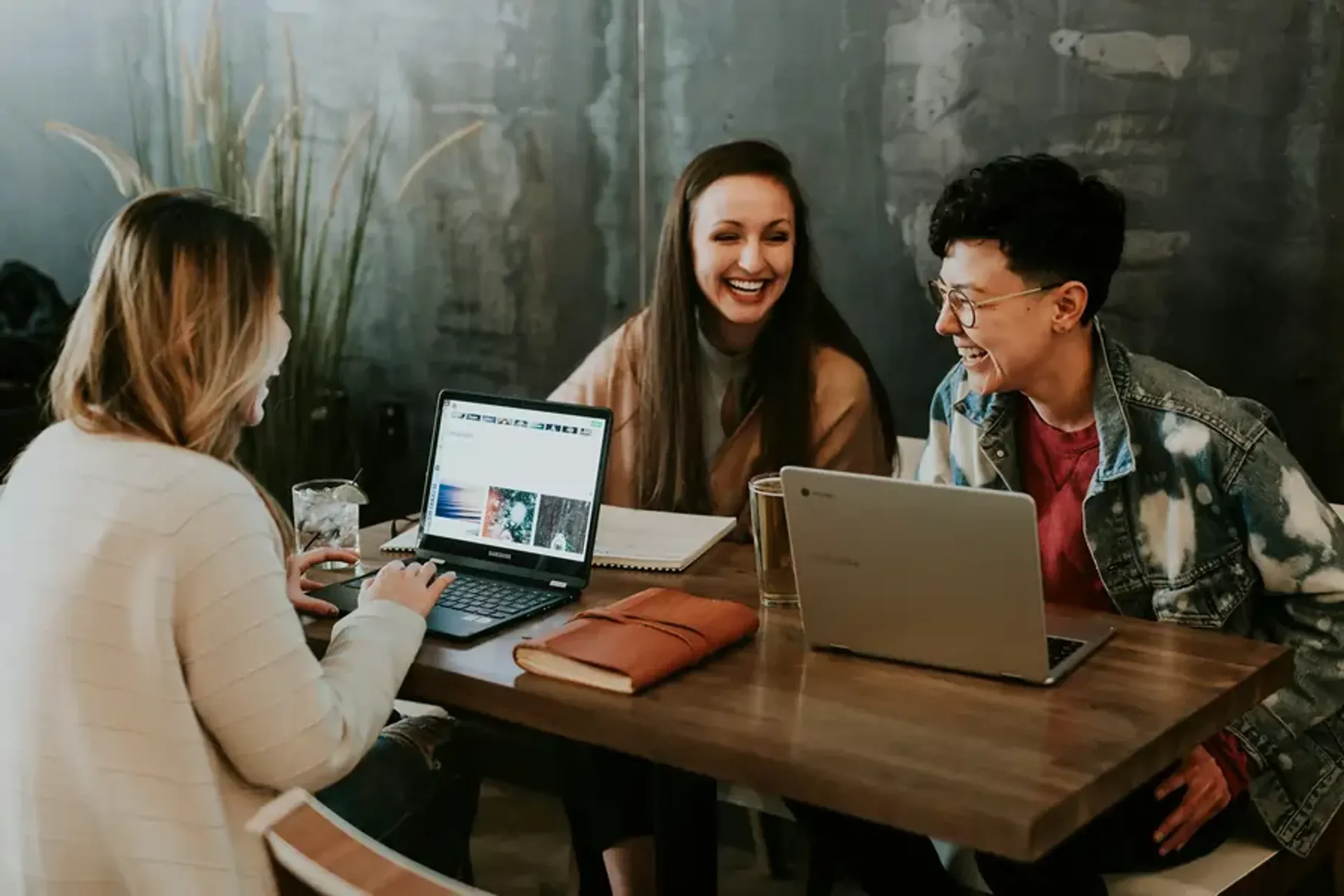 Three people laughing and working together on laptops at a table.