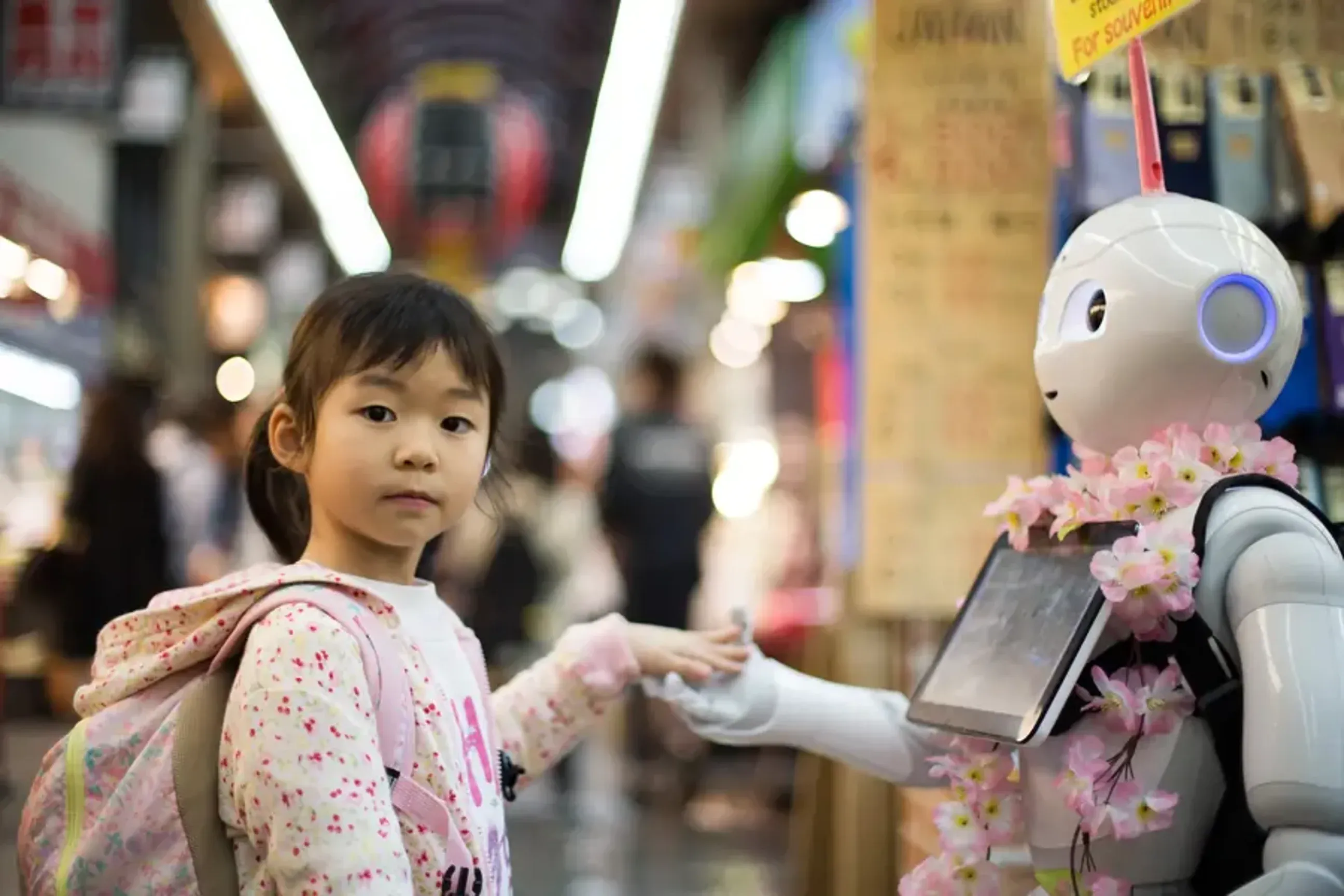 Young girl shaking hands with a service robot in a busy market.