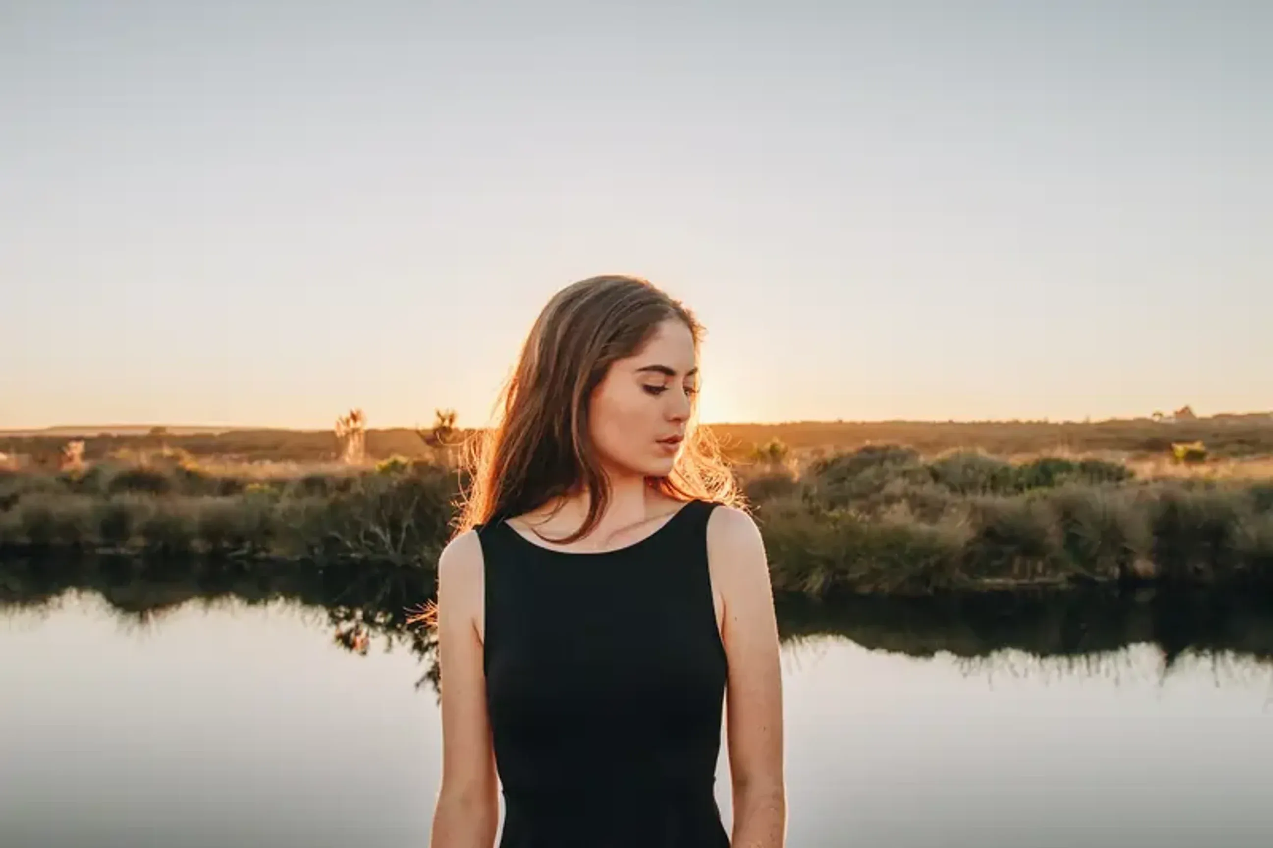 Woman standing by calm water at sunset.