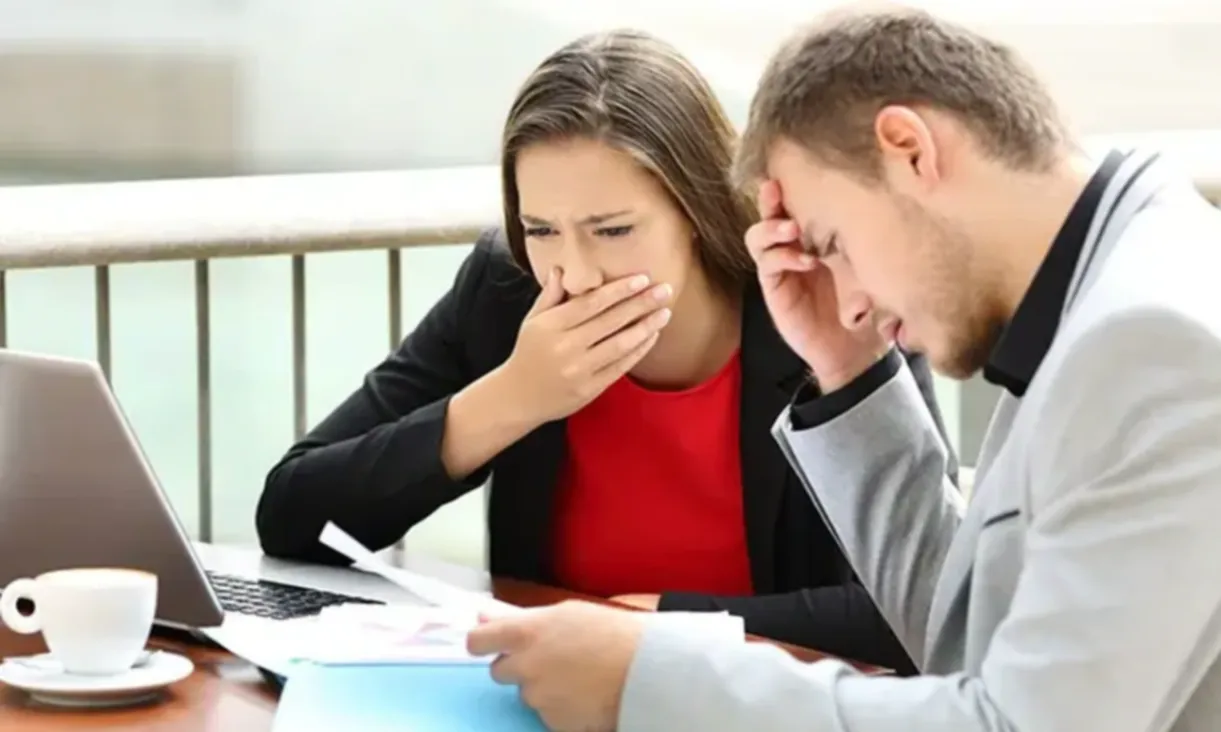 Two professionals looking worried while reviewing documents on a laptop.