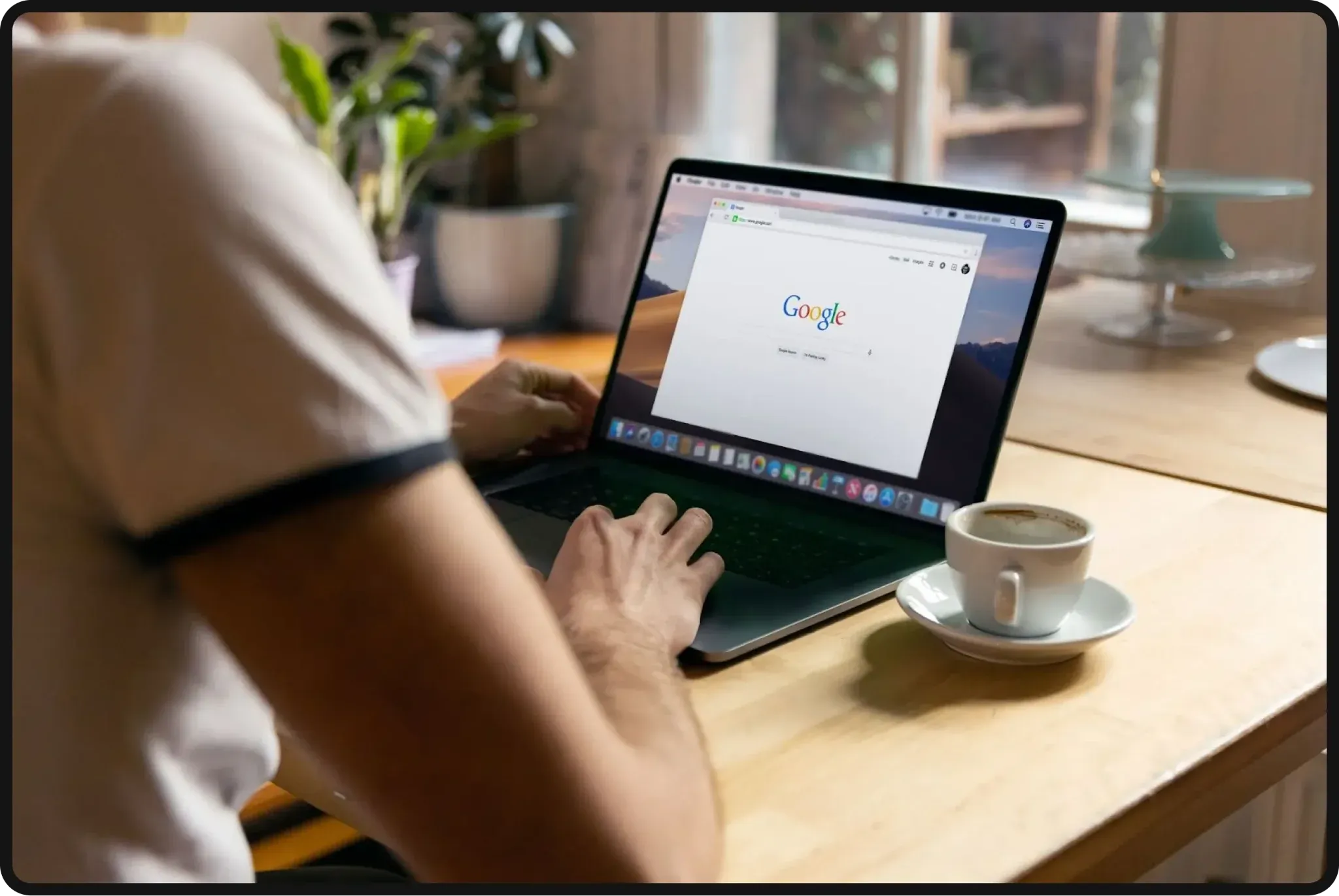 Person searching on Google on a laptop while sitting at a table with a cup of coffee.