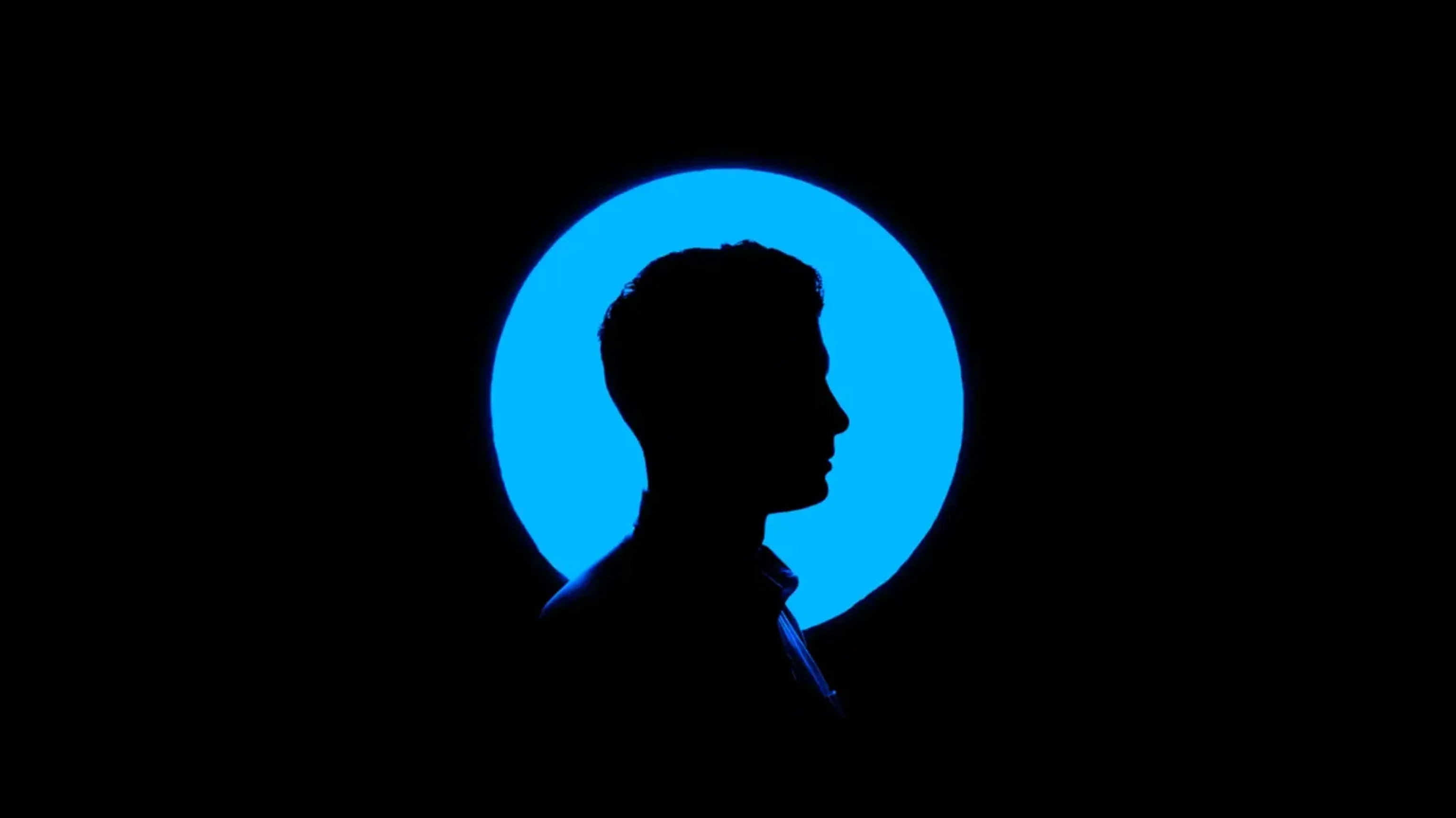 Silhouette of a man’s profile against a glowing blue circular light.